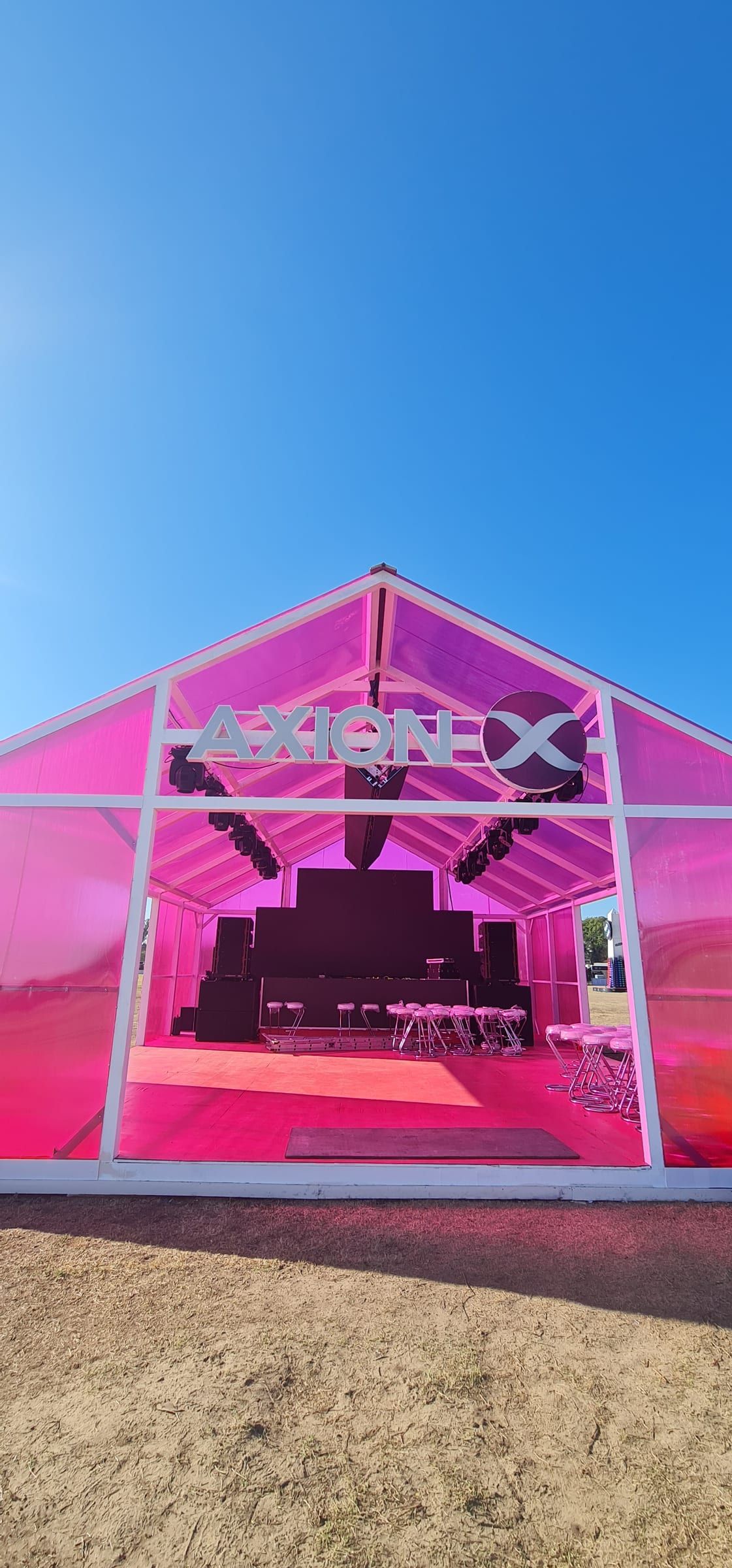 Frente del pabellón de Axion con el logo sobre la estructura de vidrio rosa