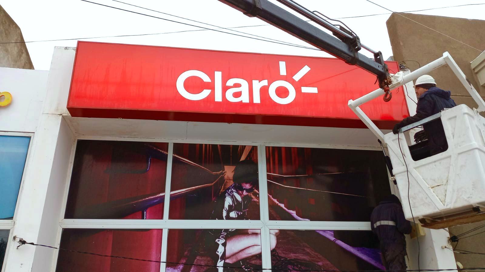 Instalación con grúa del cartel luminoso de Claro sobre una vidriera ploteada