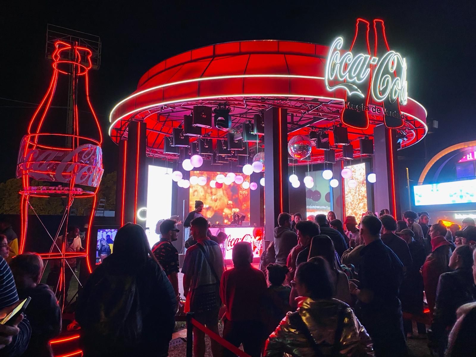 Domo de Coca-Cola de noche con la botella de neón y público frente al DJ