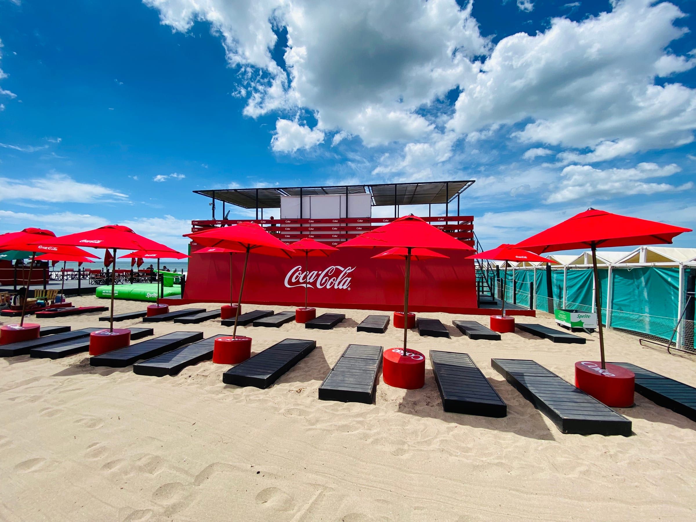 Carpa de Coca-Cola con reposeras rojas en la playa