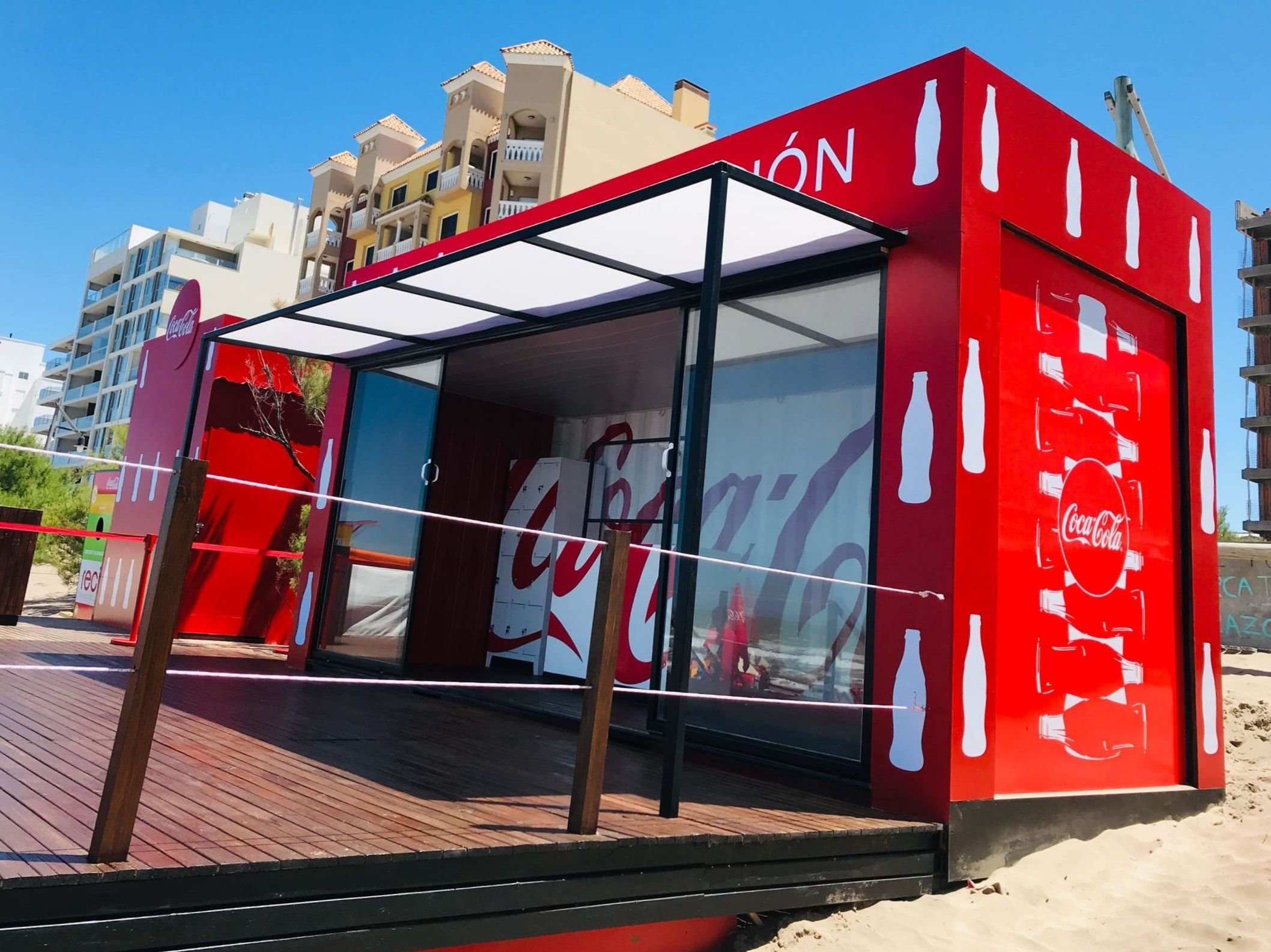 Container de Coca-Cola abierto sobre la playa, con los edificios de la costa de fondo