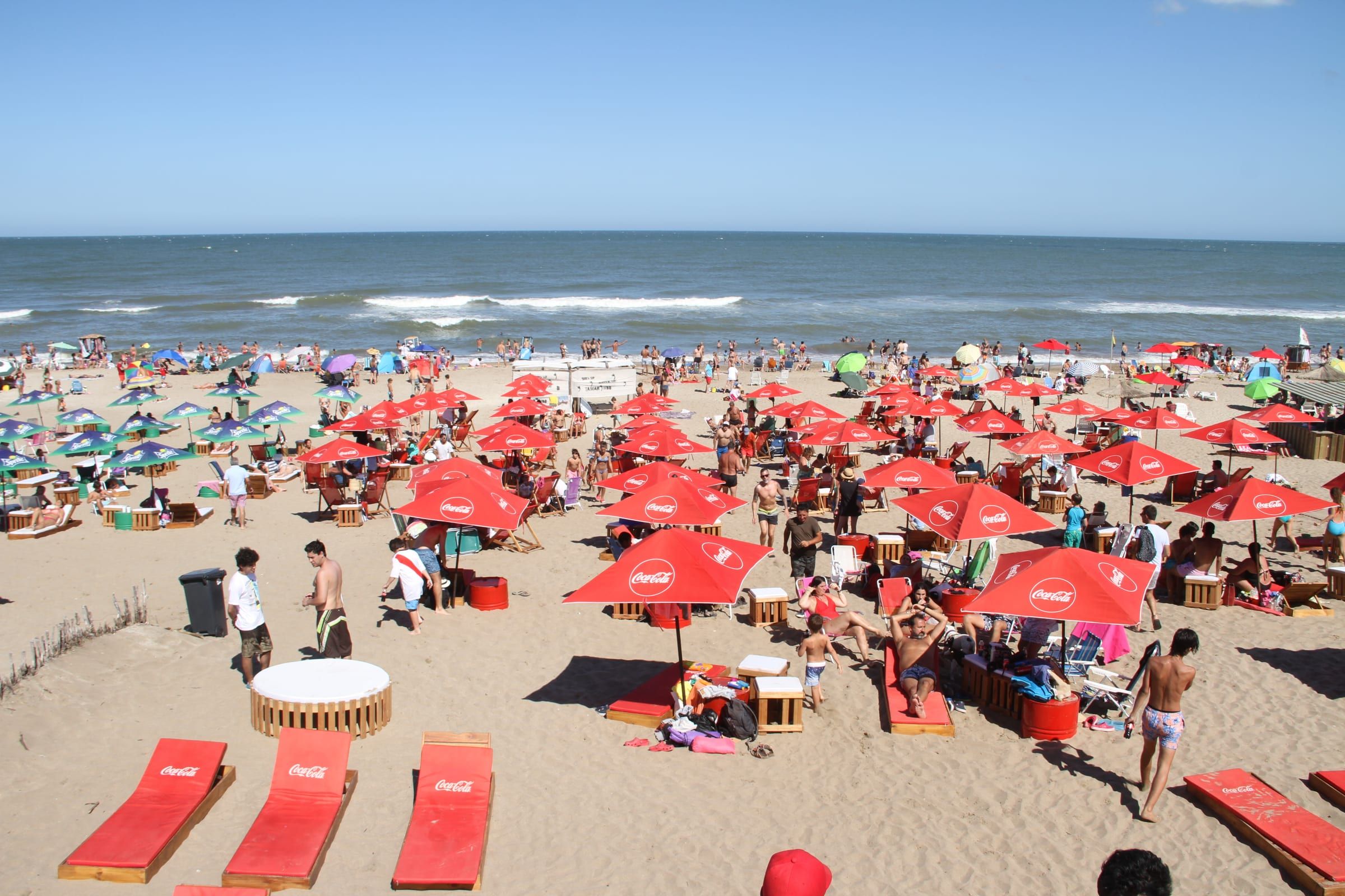 Playa cubierta de sombrillas rojas de Coca-Cola frente al mar