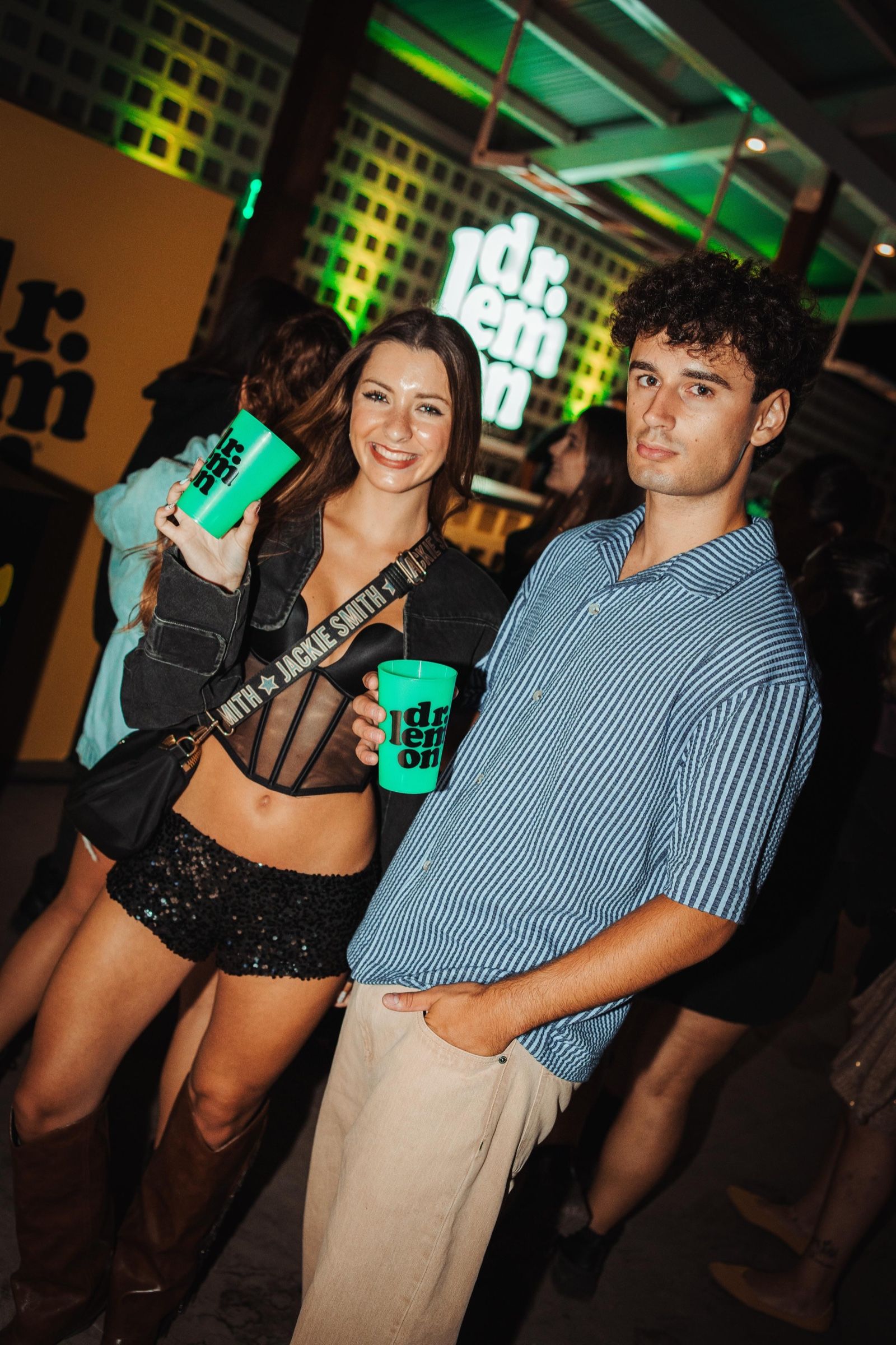 Pareja con vasos de Dr. Lemon frente al cartel iluminado de la marca