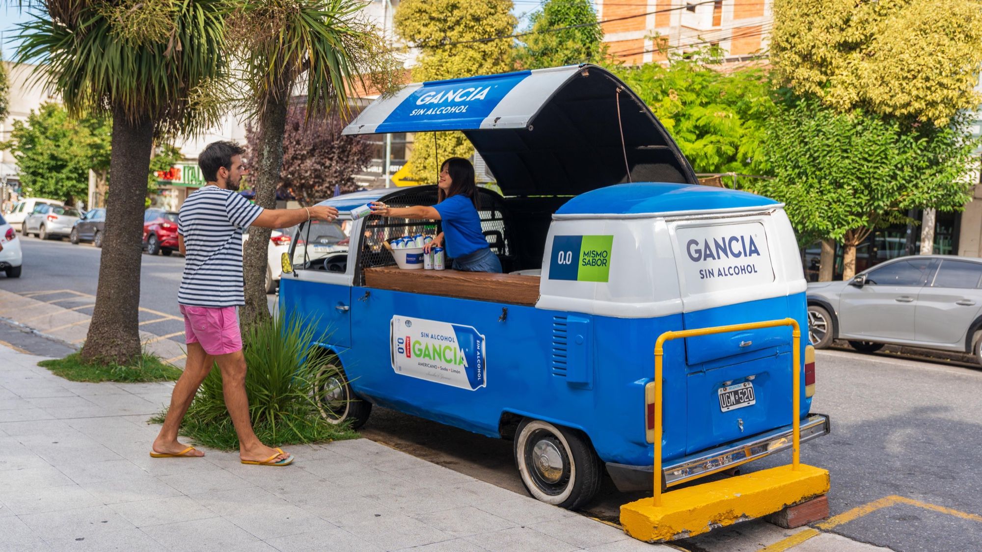 Promotora de Gancia sin alcohol entregando una lata desde una kombi azul en la calle