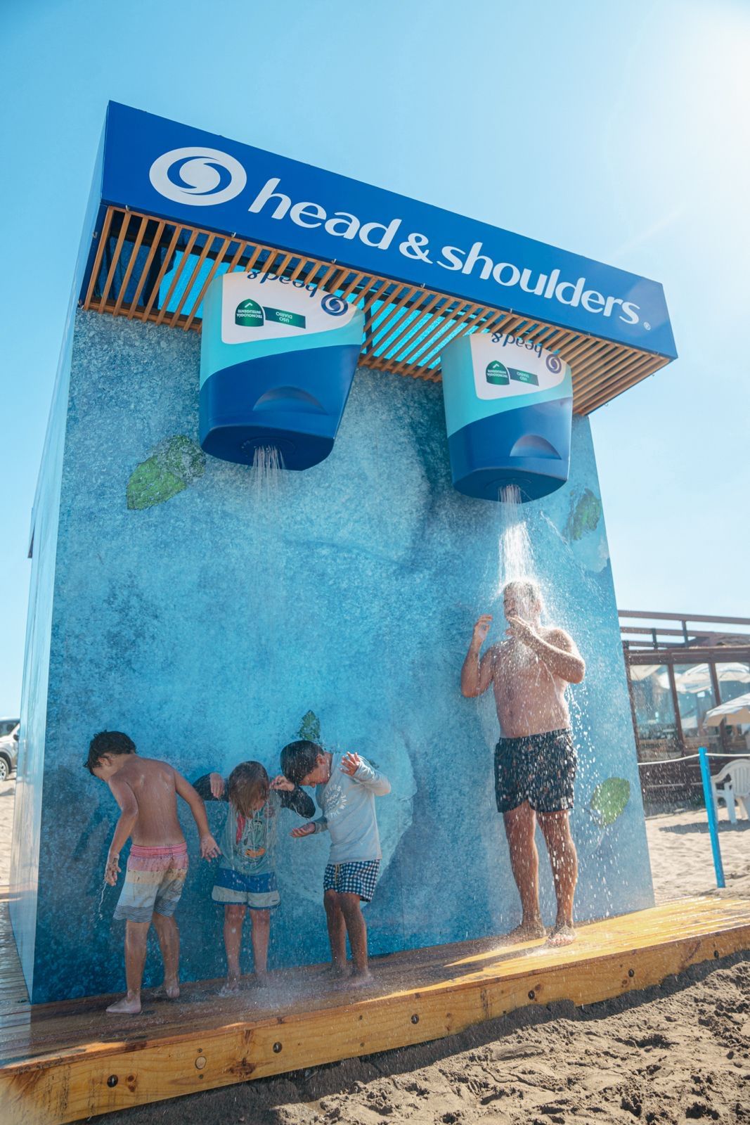 Chicos y un adulto bajo las duchas con forma de envase de Head & Shoulders