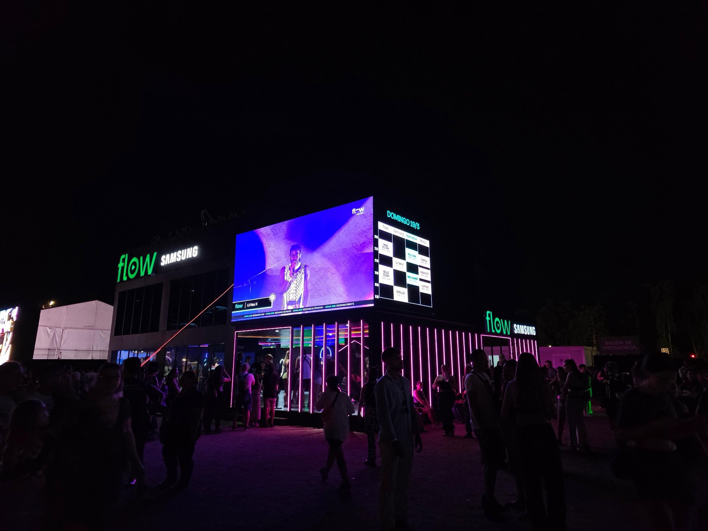 Stand de Flow iluminado de noche con el público alrededor