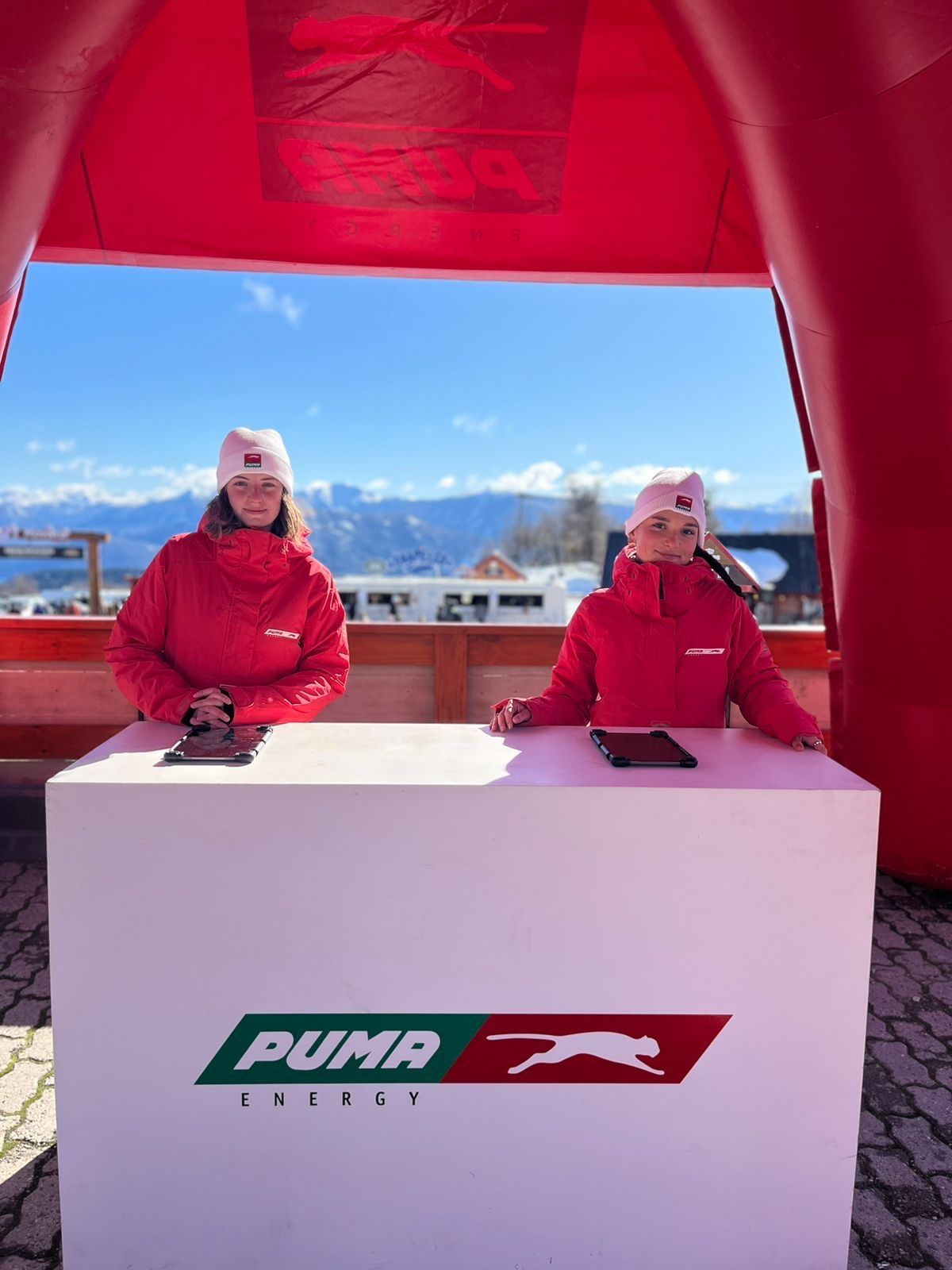 Dos promotoras de Puma Energy en la mesa de recepción, con la cordillera de fondo