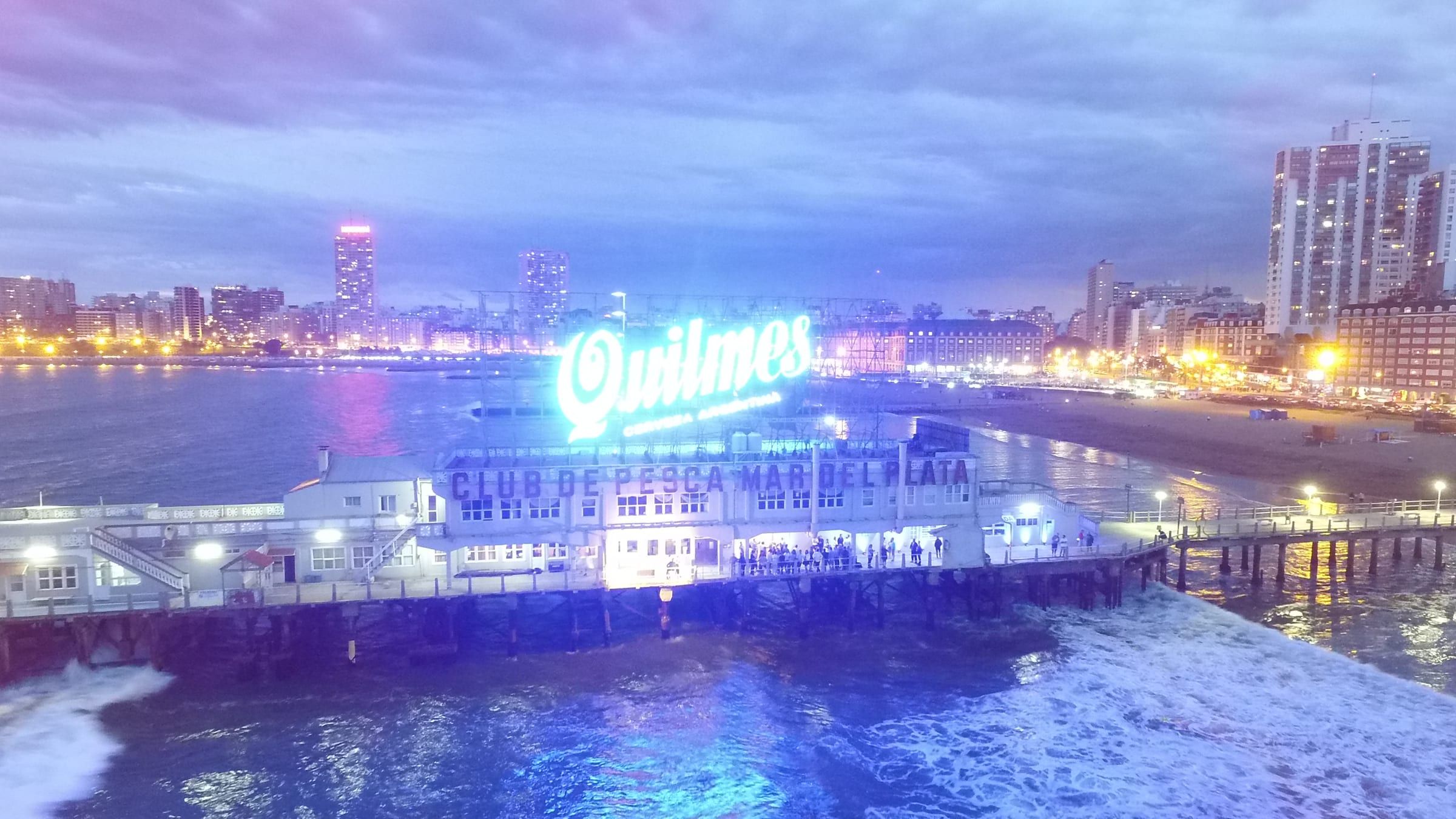 El espigón del Club de Pesca iluminado con el cartel de Quilmes y la ciudad de fondo